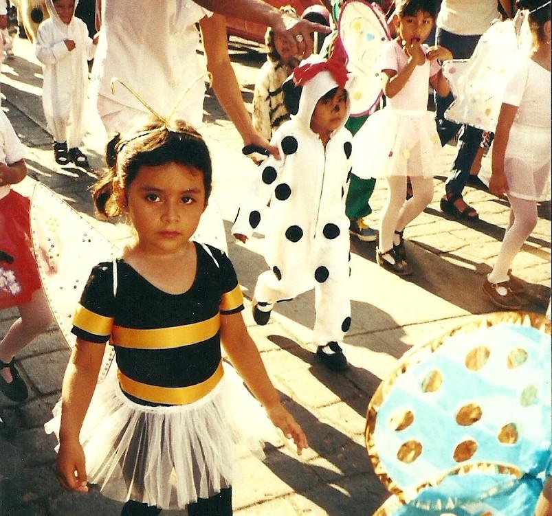 Photo of Frida Flores as a young child in a costume surrounded by other children in costumes