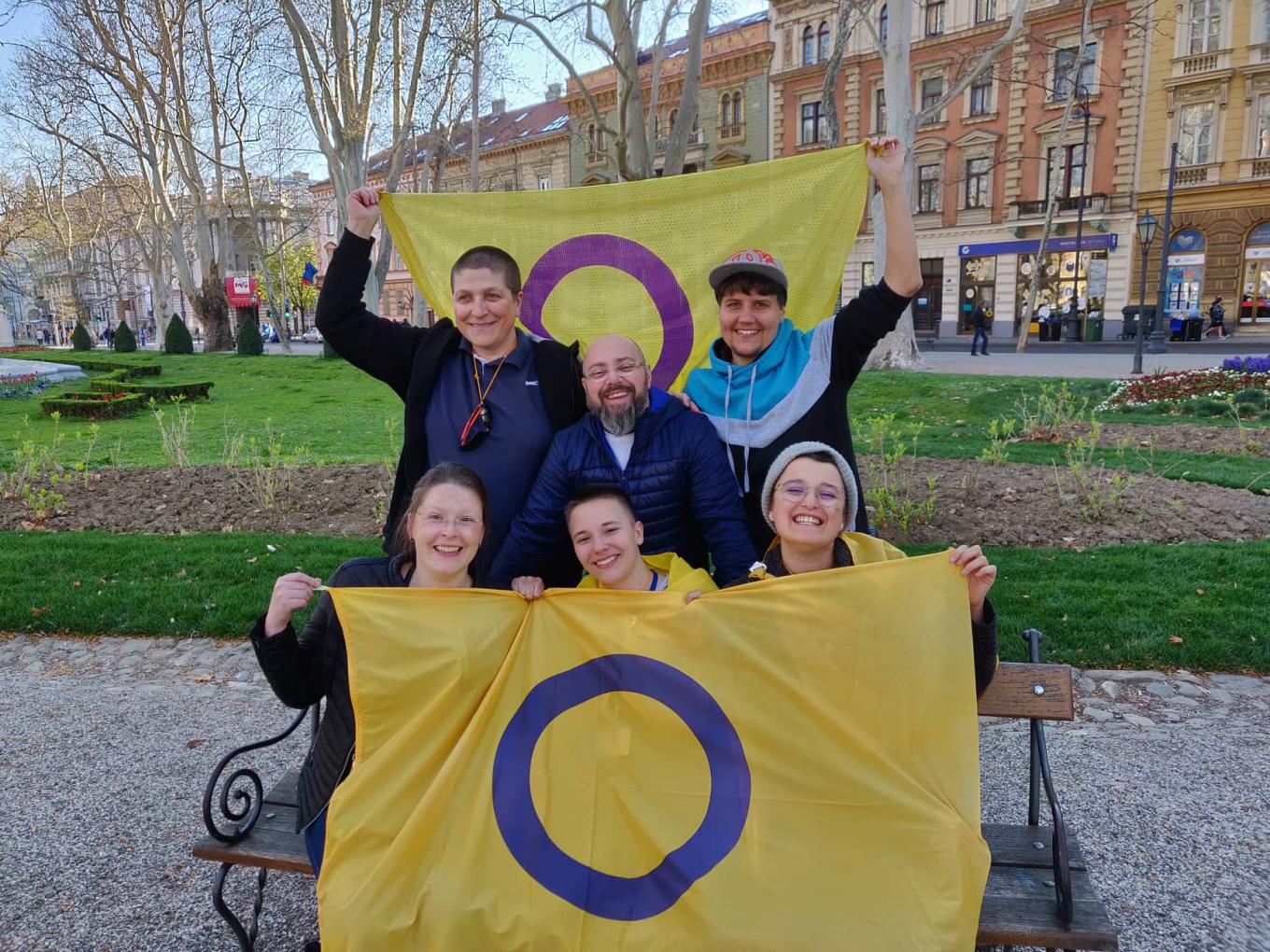 A group of people gather with two intersex flags raising their fists with pride.