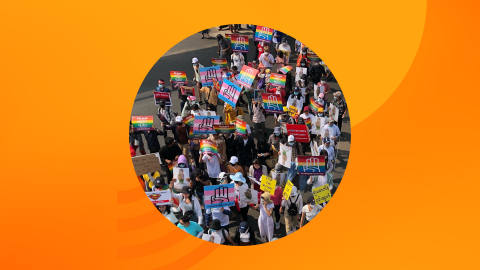 A crowd marches in Myanmar with rainbow flag and trans flag signs reading #LGBTQ4Democracy